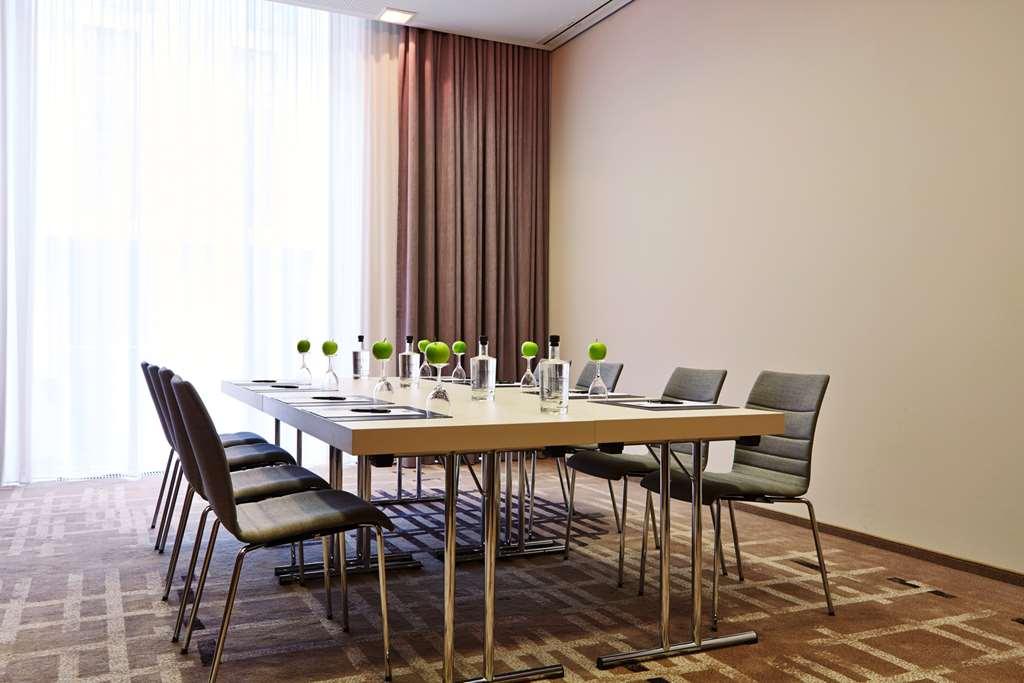 Steigenberger Hotel Am Kanzleramt Berlin Einrichtungen foto The photo shows a modern conference room. There is a large rectangular table in the center surrounded by several chairs. The table is set up for a meeting, with water pitchers and glasses placed on it, along with small green decorative plants. The ro