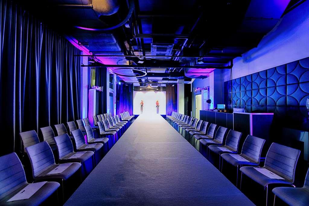 Steigenberger Hotel Am Kanzleramt Berlin Einrichtungen foto The photo shows a fashion runway setup. There's a long, narrow runway stretching down the center, flanked by rows of modern chairs on either side. The space is dimly lit, with dramatic purple and blue lighting creating an atmosphere suited for a fash