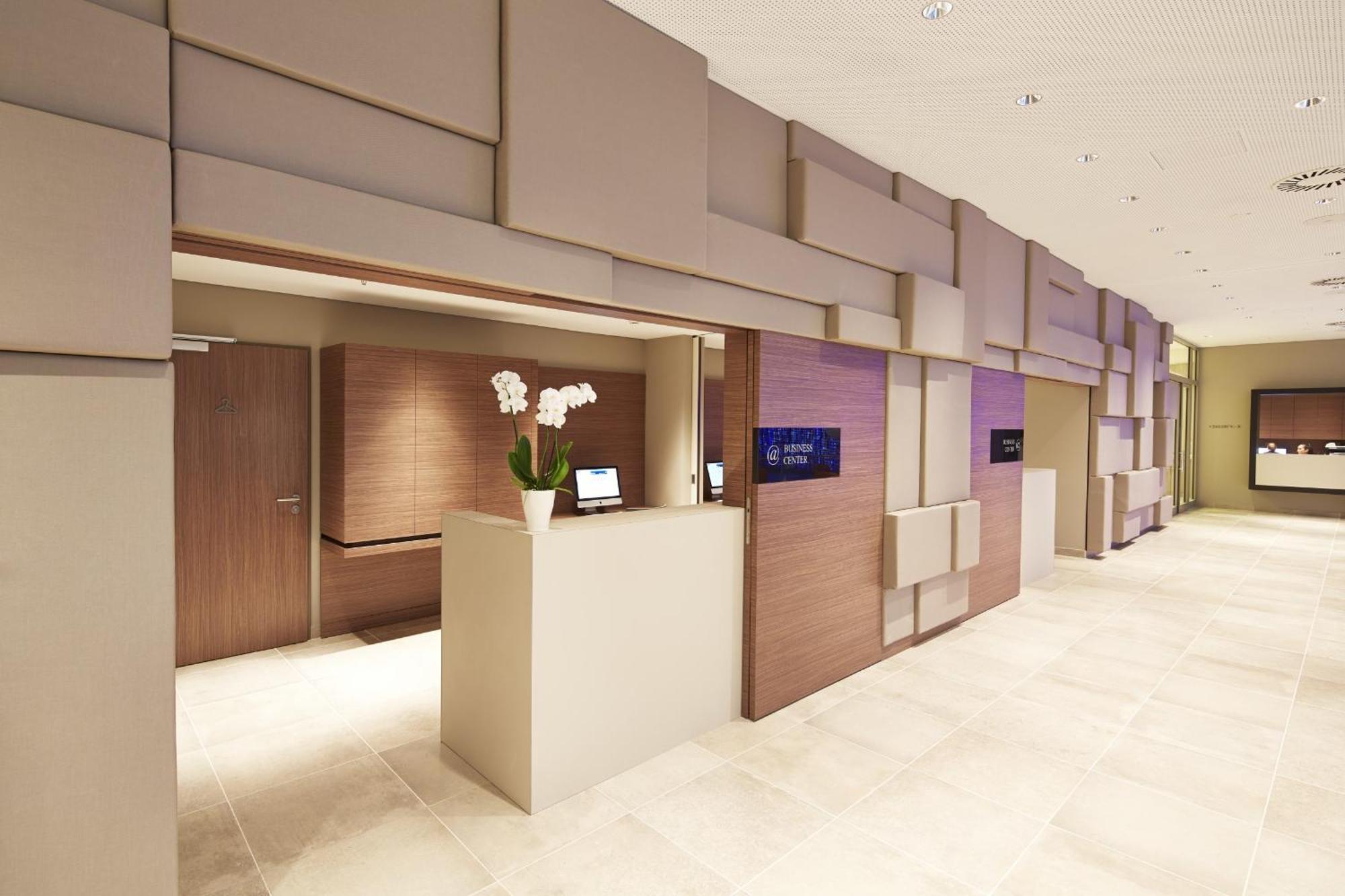 Steigenberger Hotel Am Kanzleramt Berlin Exterior foto The photo shows a modern reception area with a sleek design. The walls are decorated with a mix of beige and brown panels that create a textured appearance. To the left, there is a reception desk with a minimalist style, featuring a small plant with 