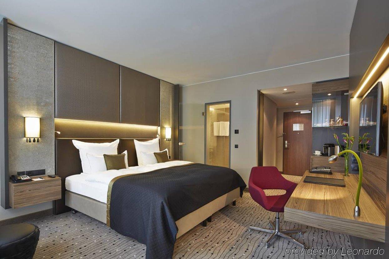 Steigenberger Hotel Am Kanzleramt Berlin Exterior foto The photo shows a modern hotel room featuring a neatly made bed with a dark-colored bedspread. There are two white pillows positioned at the head of the bed. The room has walls with a neutral color palette and stylish lighting, adding an elegant touc