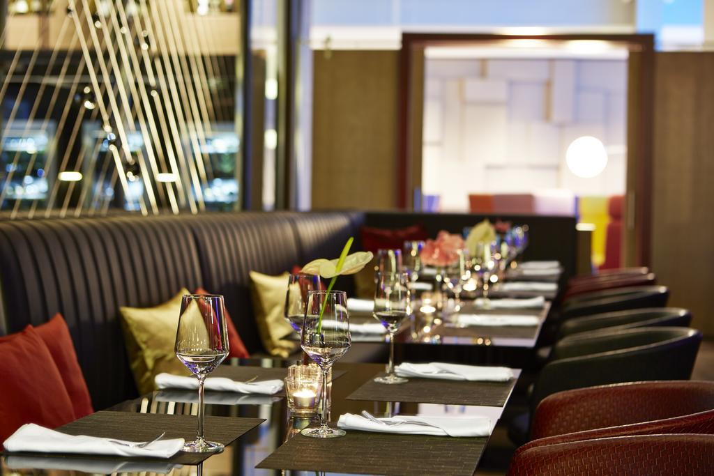 Steigenberger Hotel Am Kanzleramt Berlin Exterior foto The photo shows the interior of a restaurant. There are elegantly set tables arranged in rows, each featuring a wine glass, a folded napkin, and a small decorative item, possibly a flower. The seating includes dark leather banquettes and red chairs. 