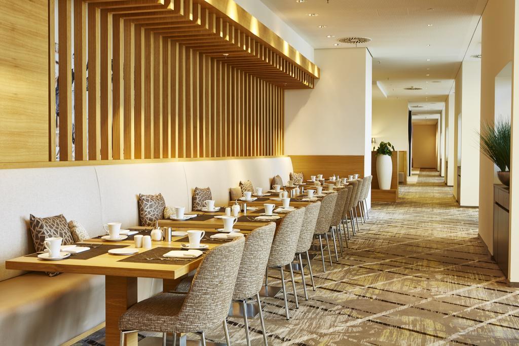 Steigenberger Hotel Am Kanzleramt Berlin Exterior foto The photo depicts a modern dining area in a restaurant. There are several long tables set with dishes, utensils, and cups, indicating that the space is prepared for dining. The chairs are upholstered and arranged neatly around the tables. The design 